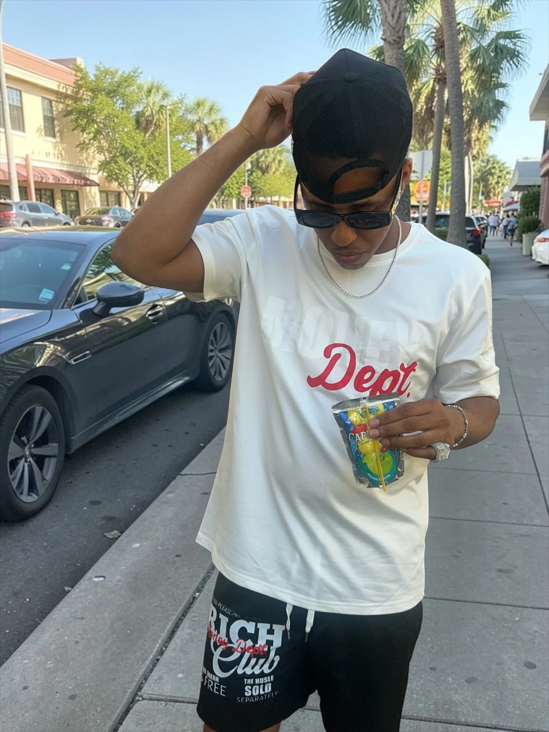 Doe Bwoy posing on a sunny sidewalk in a white graphic shirt and black shorts